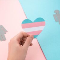 Hand holding a paper heart with transgender pride flag